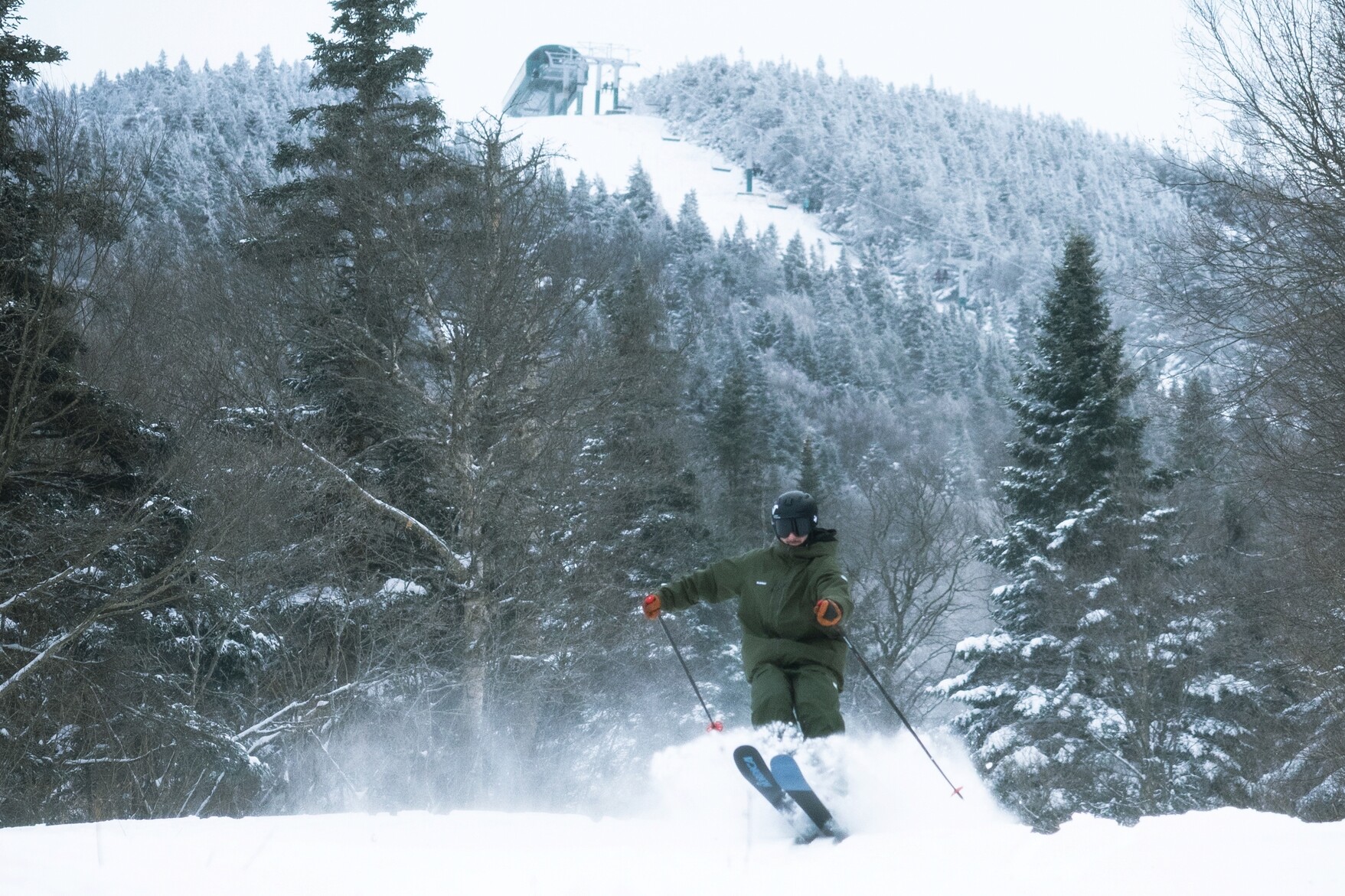 A skier navigating powder snow with a ski lift visible in the background.