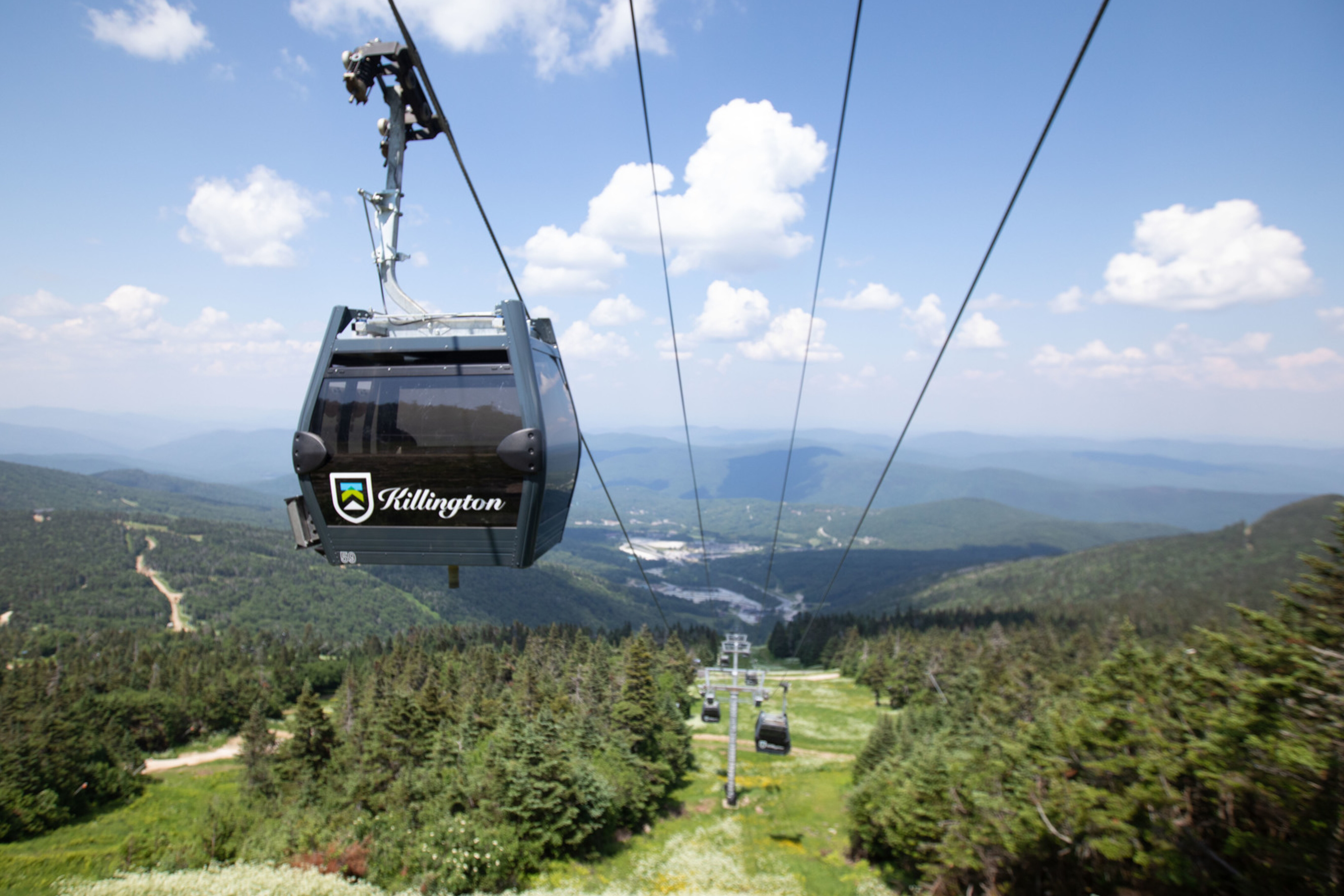 A gondola lifts over green mountains and valleys under a blue sky at Killington.