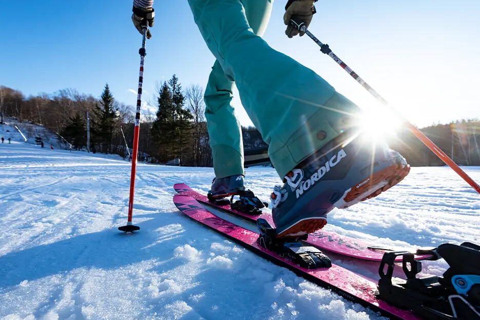Skier on pink skis with poles, sun shining behind them on a snowy slope.