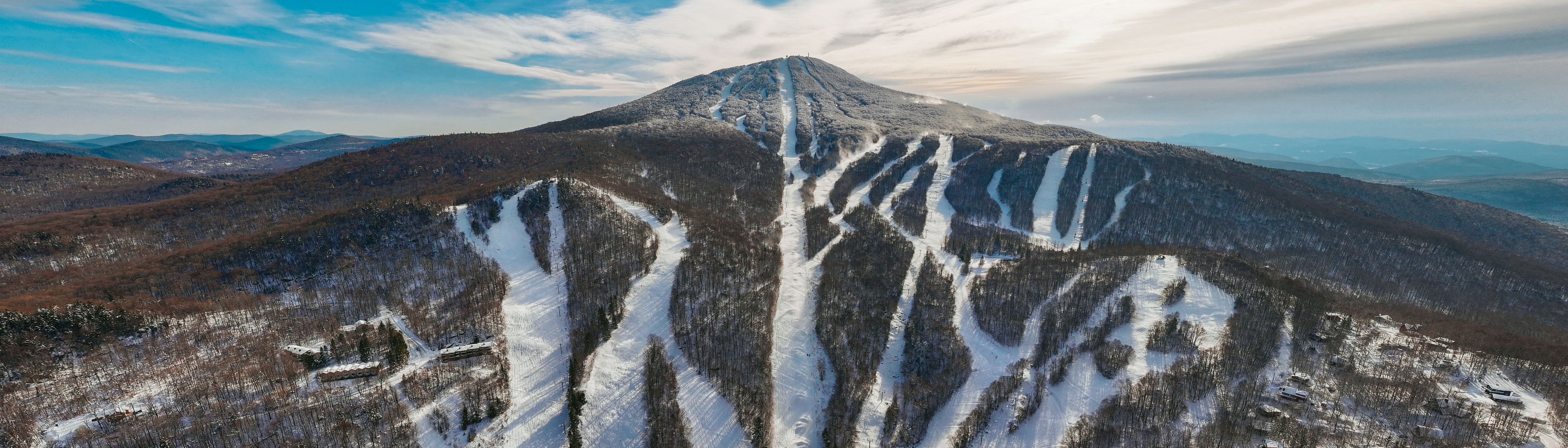 A snowy mountain landscape with ski trails and a backdrop of rolling hills.