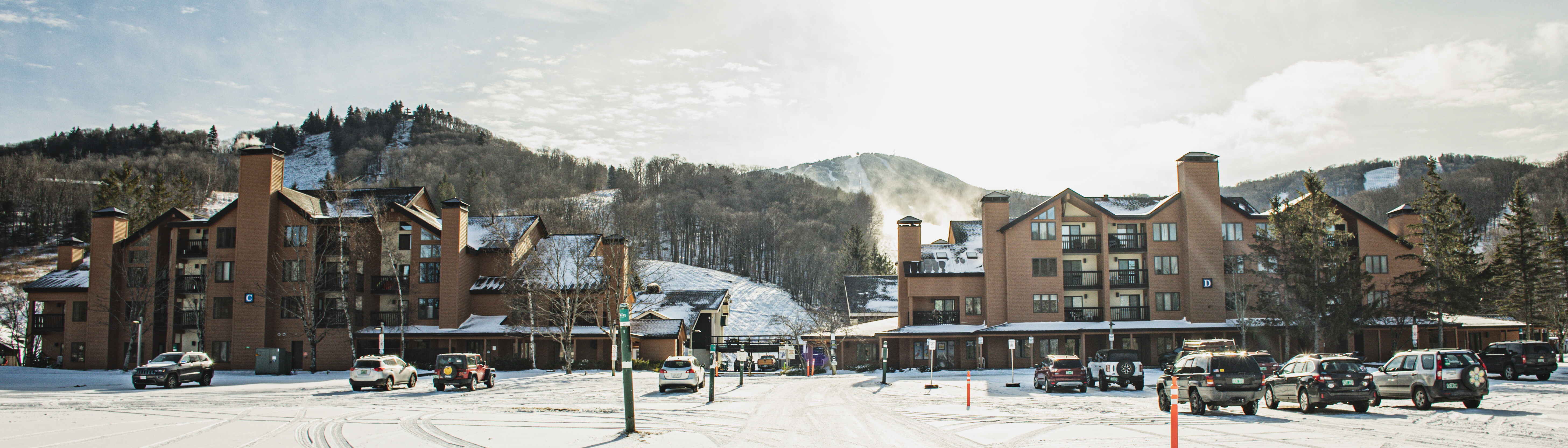 Snow-covered resort buildings with parked cars and mountains in the background.