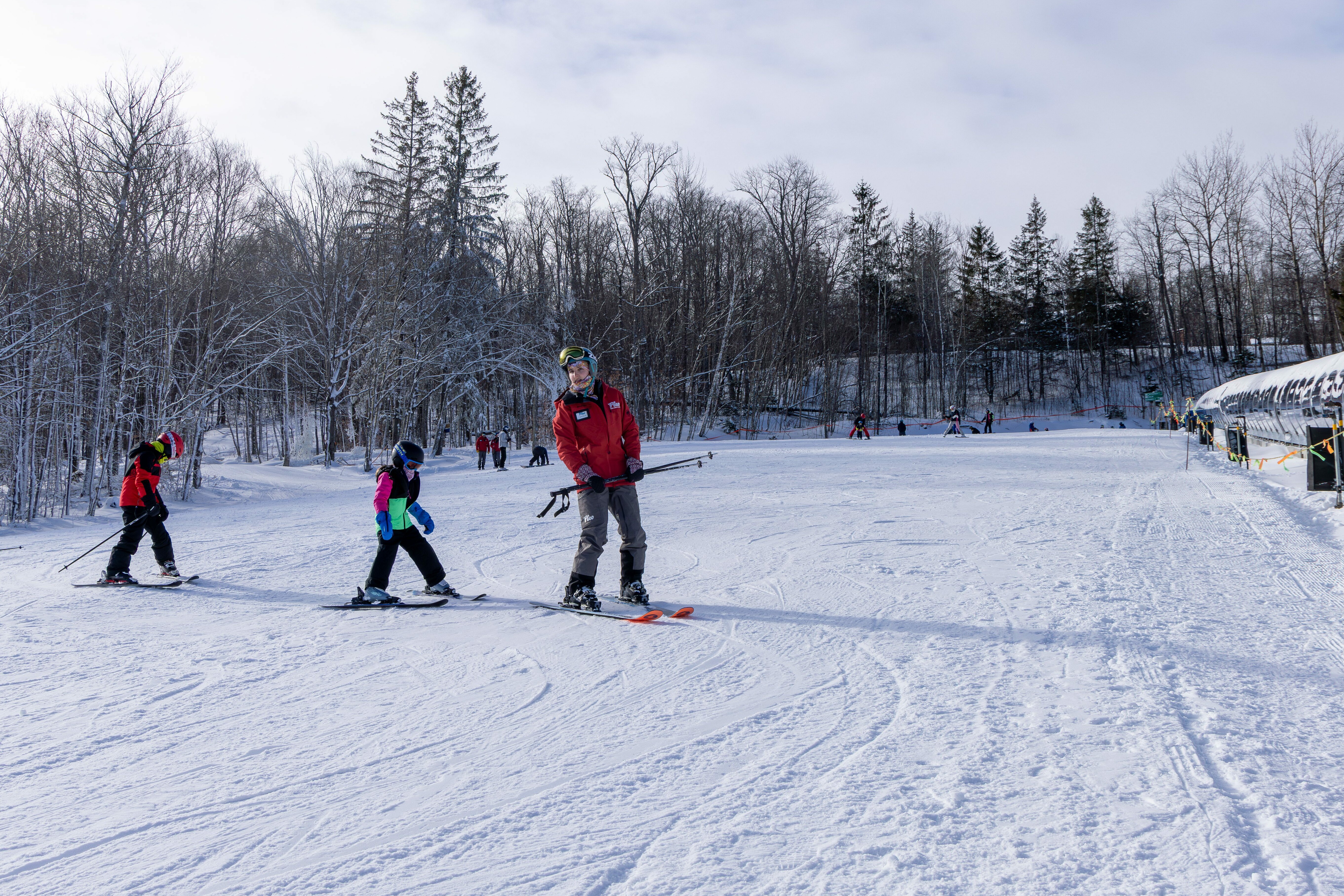 Skiers on a snowy slope, with an instructor helping a child in colorful gear.