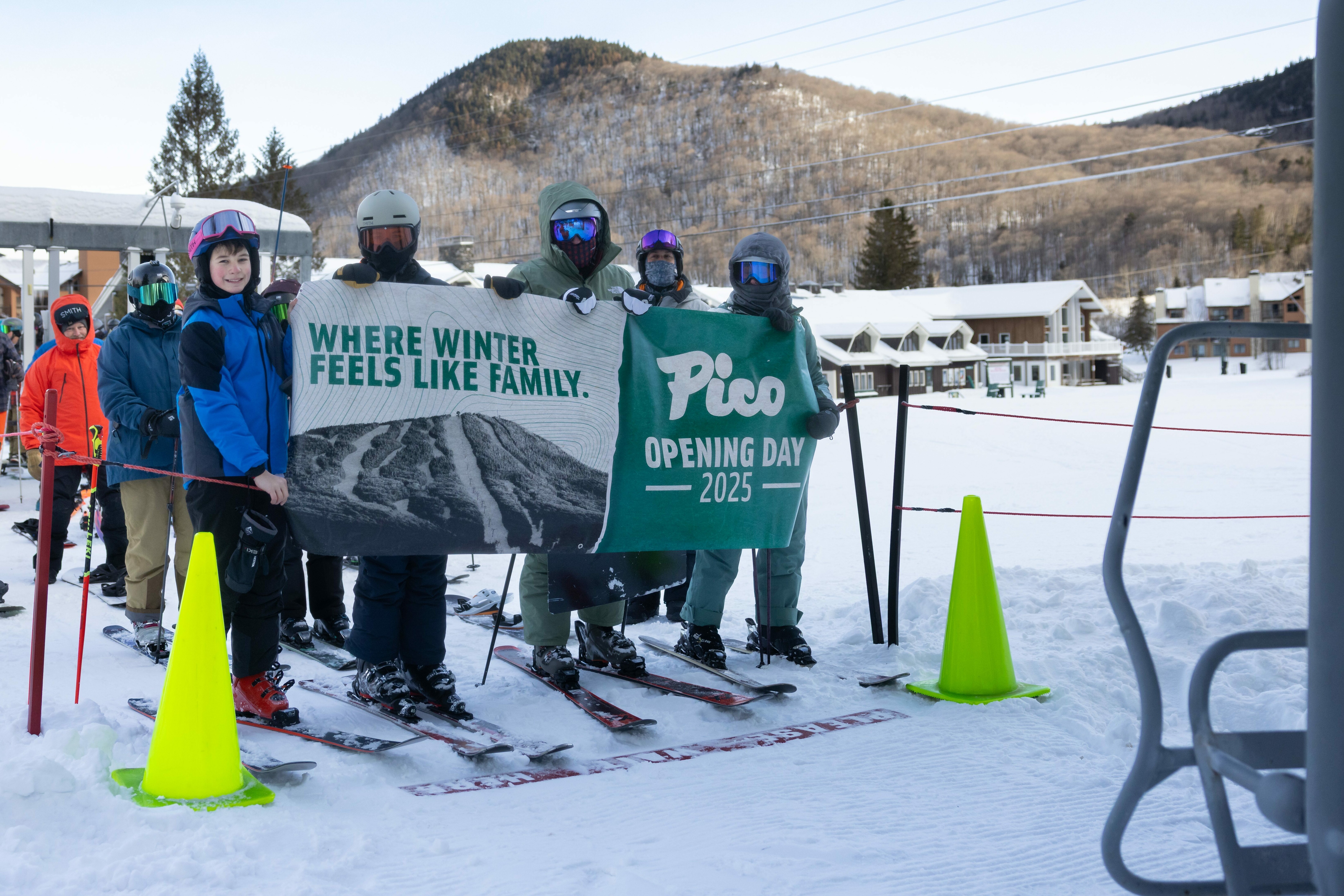 Skiers hold a banner for Pico's Opening Day 2025 in a snowy mountain setting.