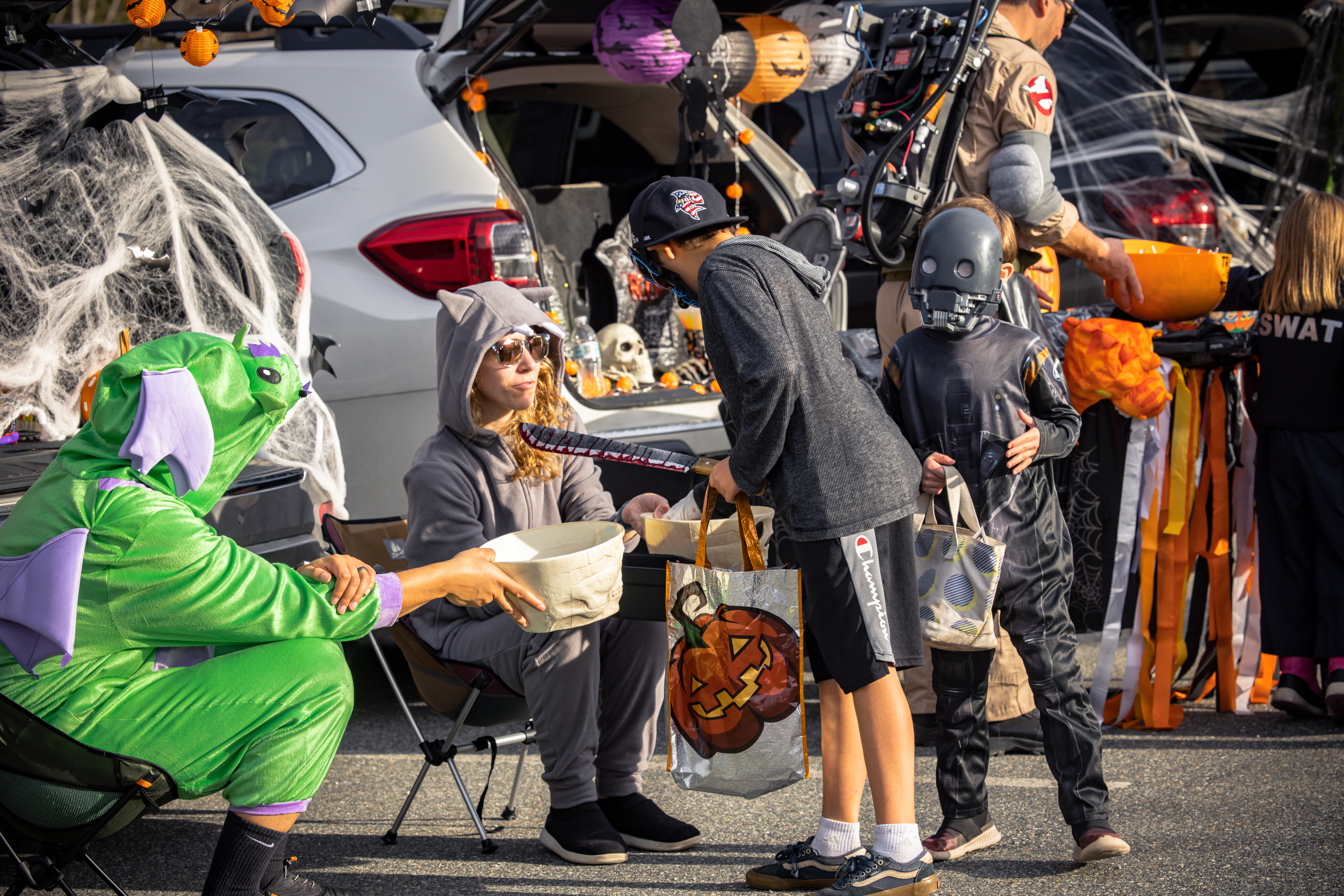Kids in costumes trick-or-treating at a decorated car trunk during Halloween festivities.
