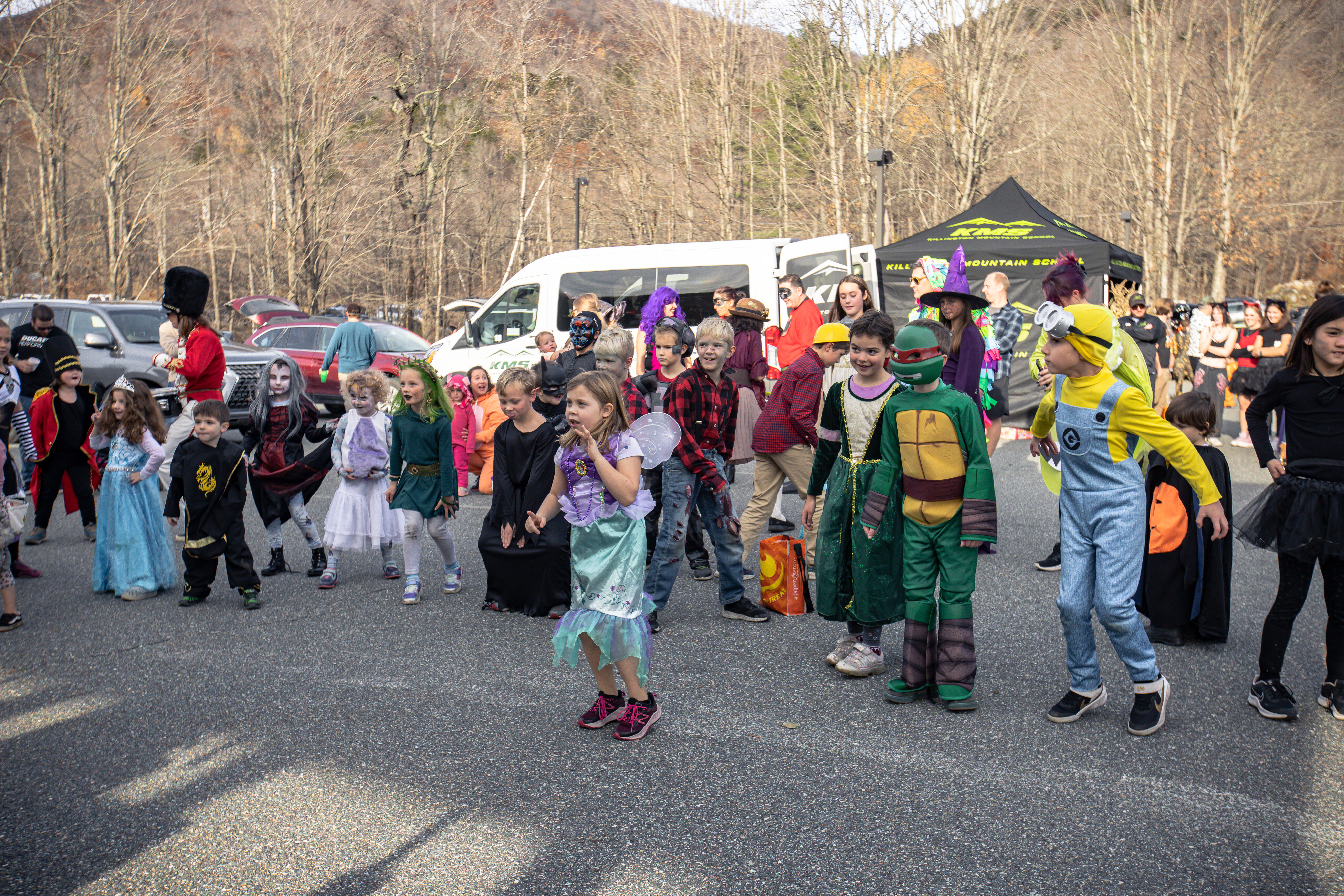 Children in various costumes dance together at an outdoor event.