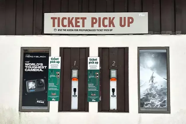 Kiosk ticket pick-up area with two machines and a sign indicating usage instructions.