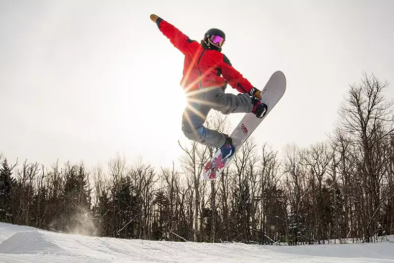 Snowboarder mid-air performing a jump with sunlight shining behind them.