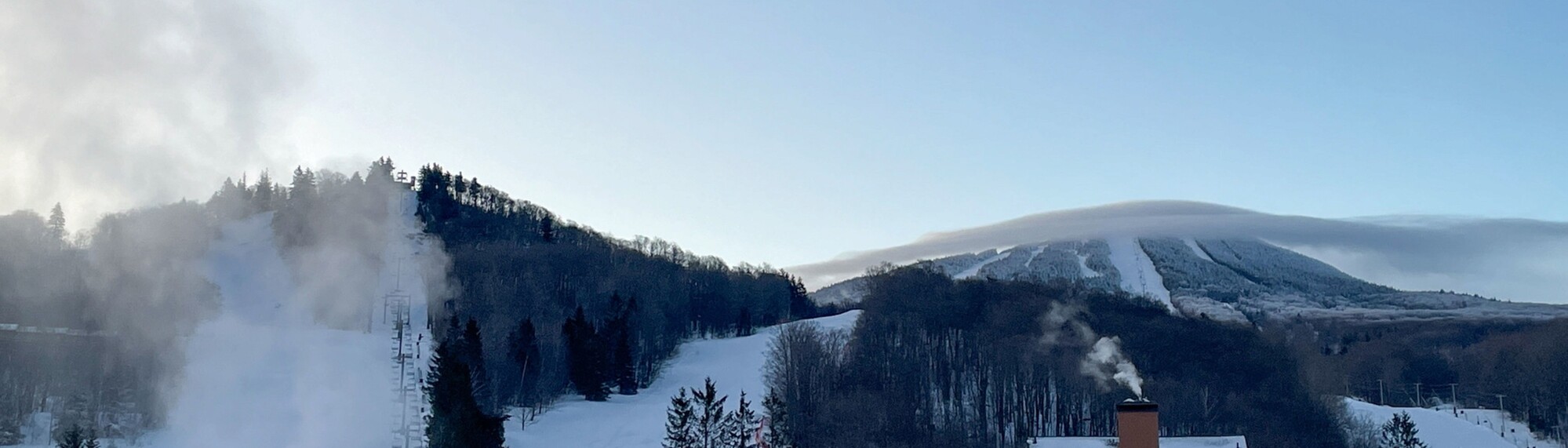 Snow-covered mountains under a clear blue sky with steam rising from nearby structures.