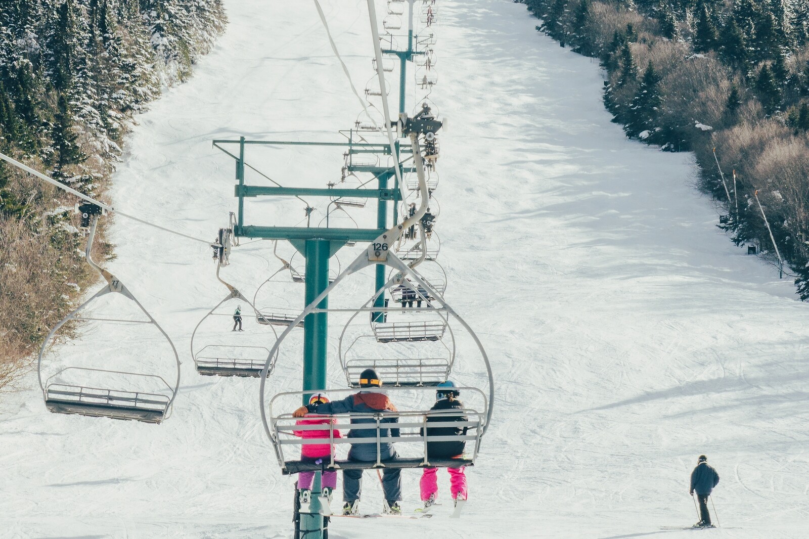 Skiers on a chairlift overlooking a snow-covered slope and trees.