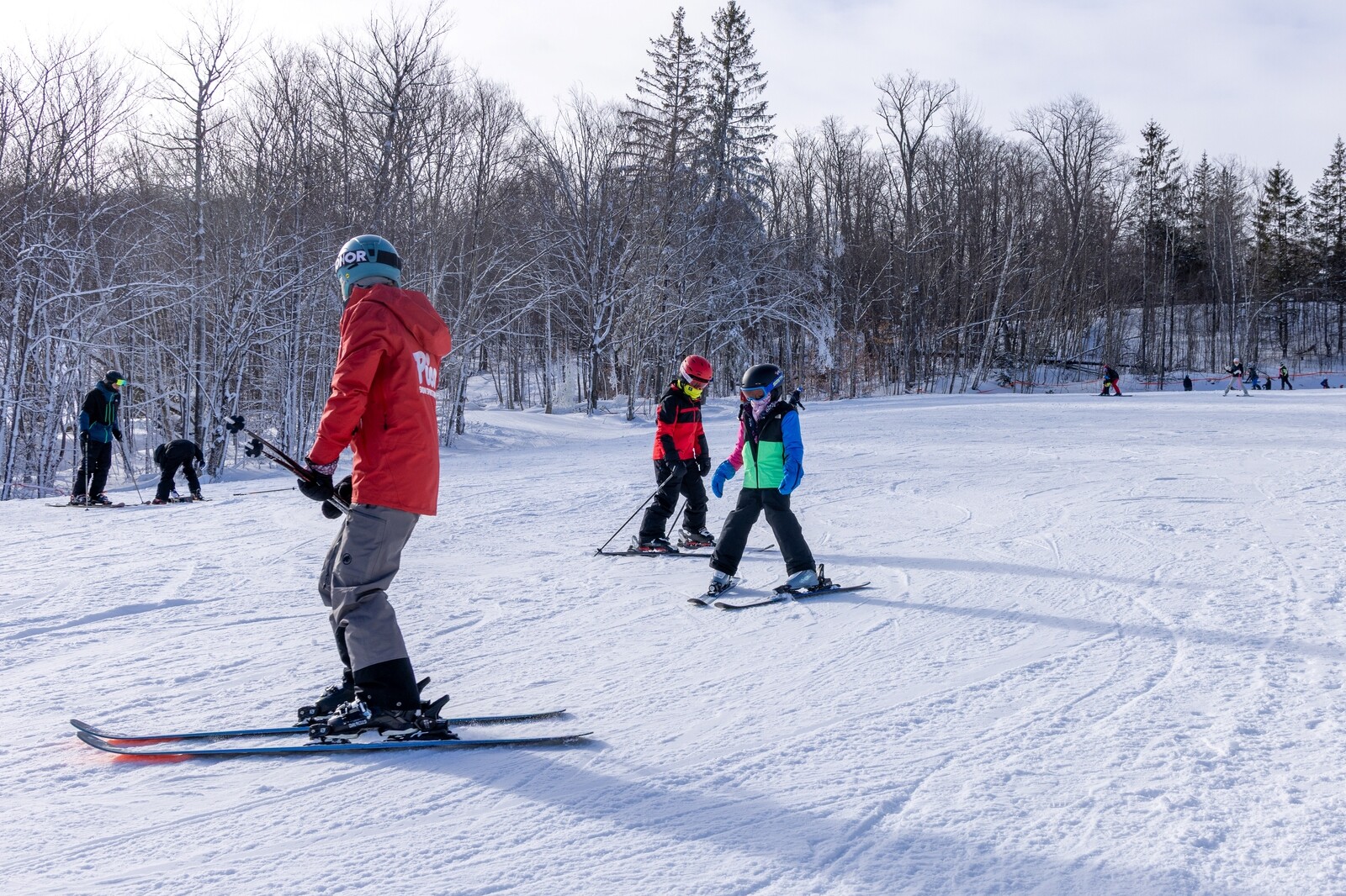 Skiers on a snowy slope, including a child and an instructor in bright jackets.