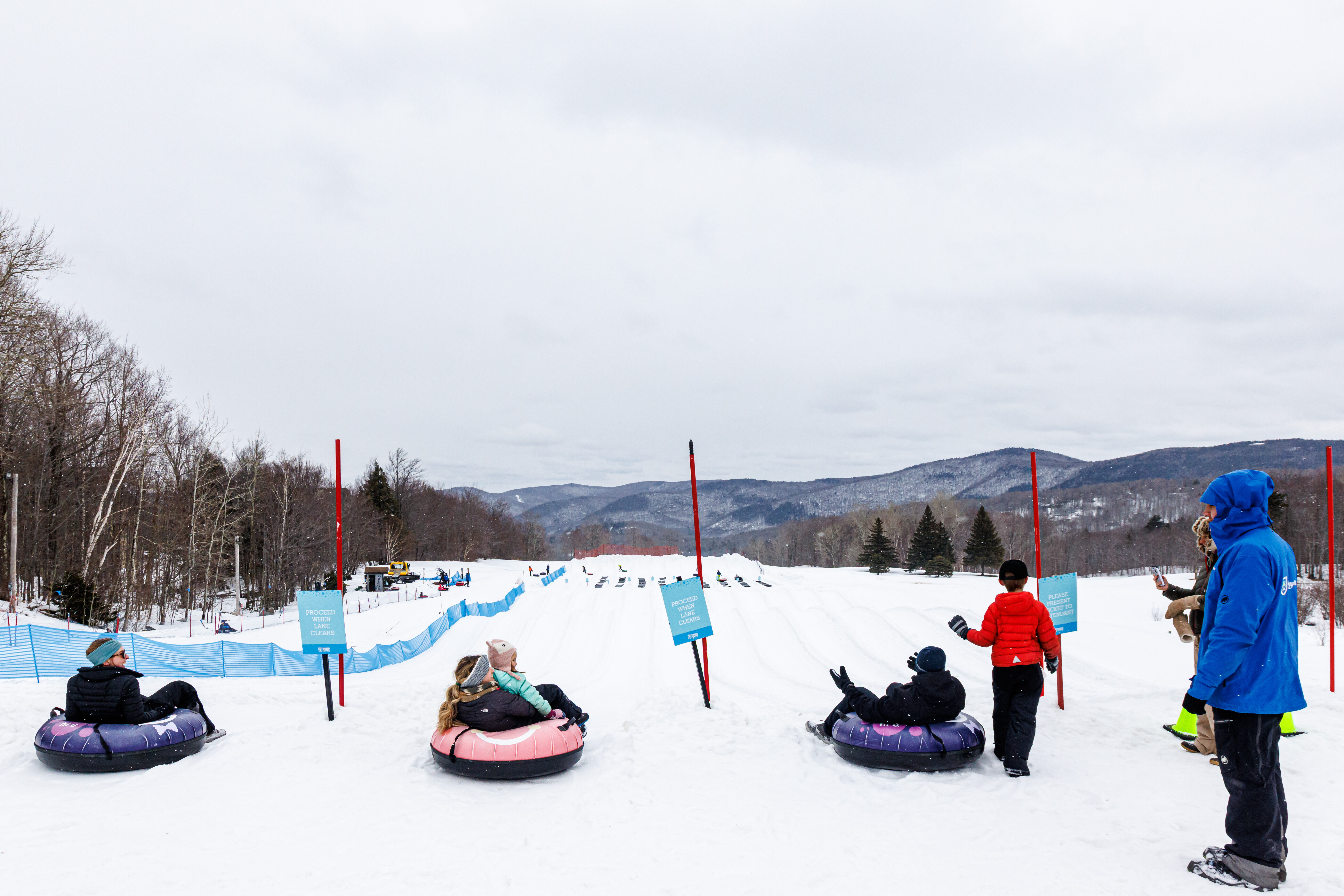 Group of people on snow tubes at a winter tubing hill with mountains in the background.