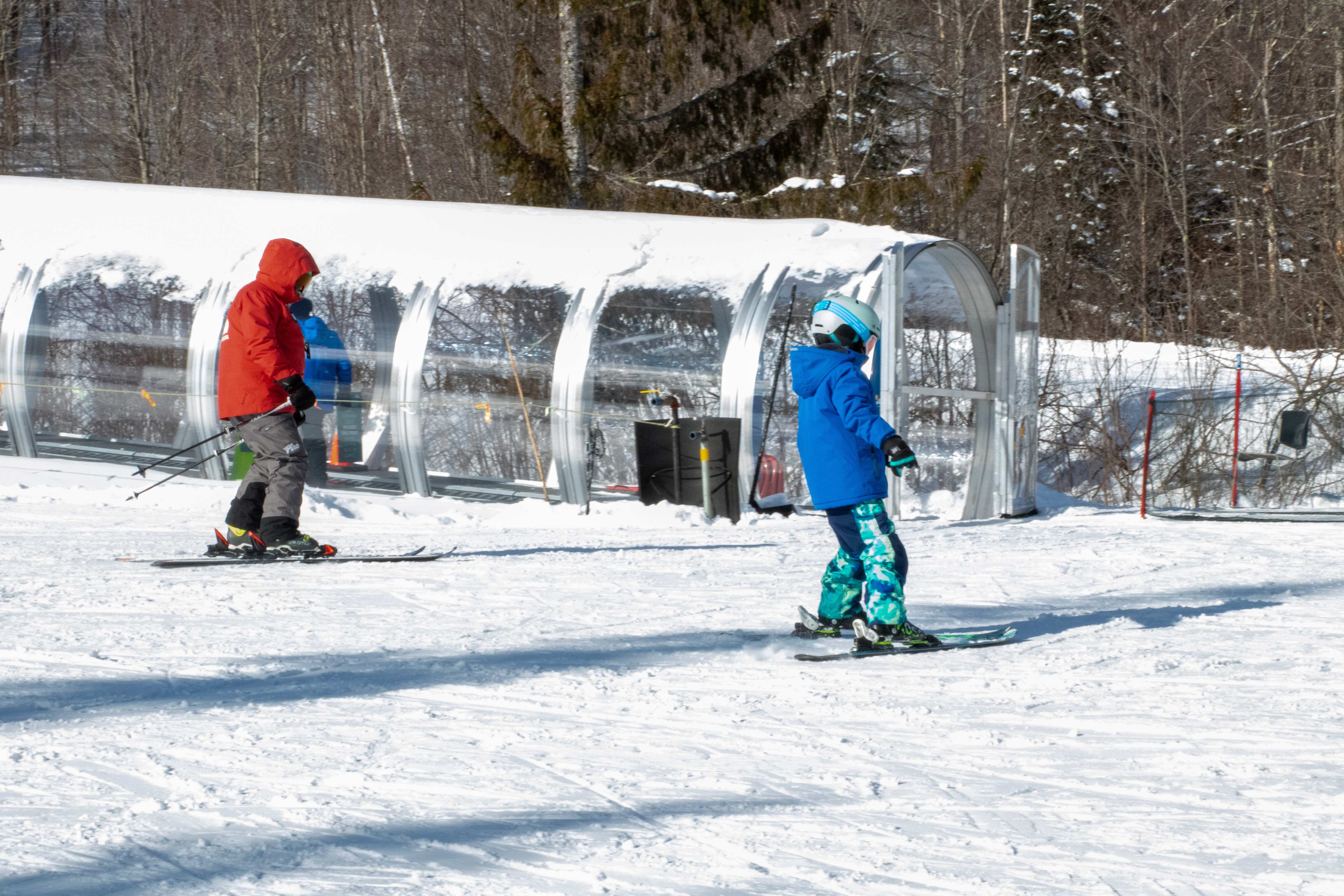 A skier in a red jacket guides a child in blue ski gear on a snowy slope.