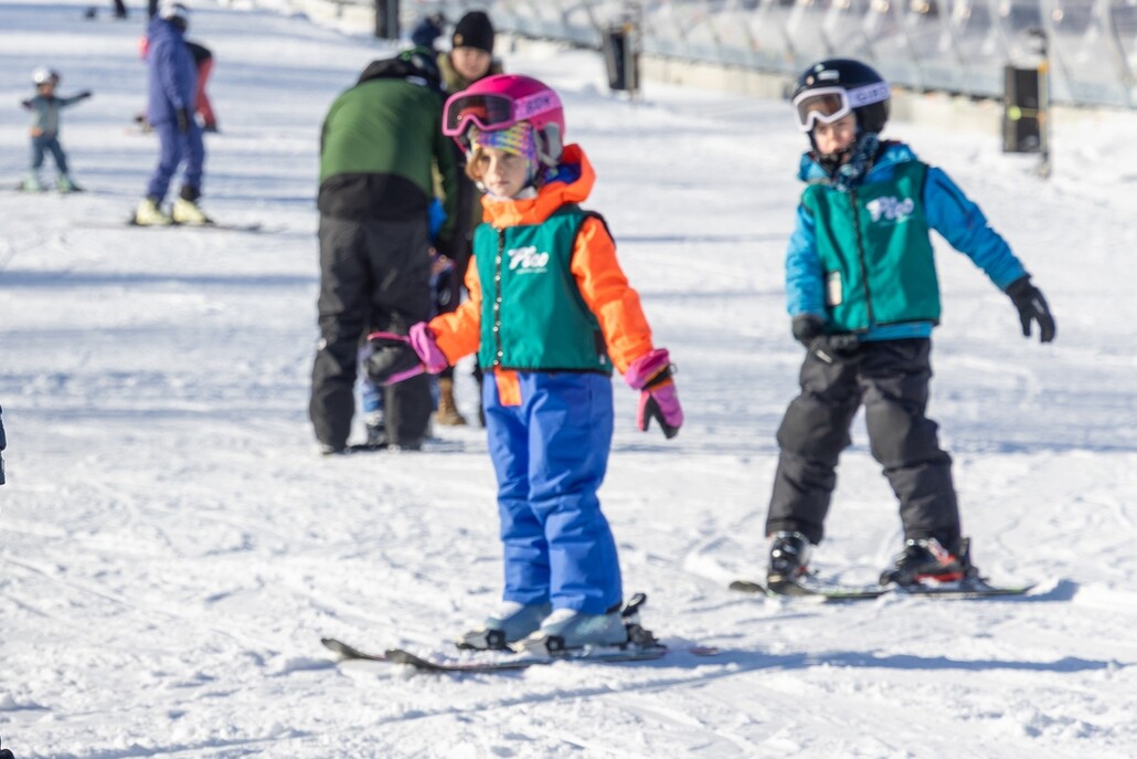 Children learning to ski on a snowy slope, wearing colorful ski gear and helmets.