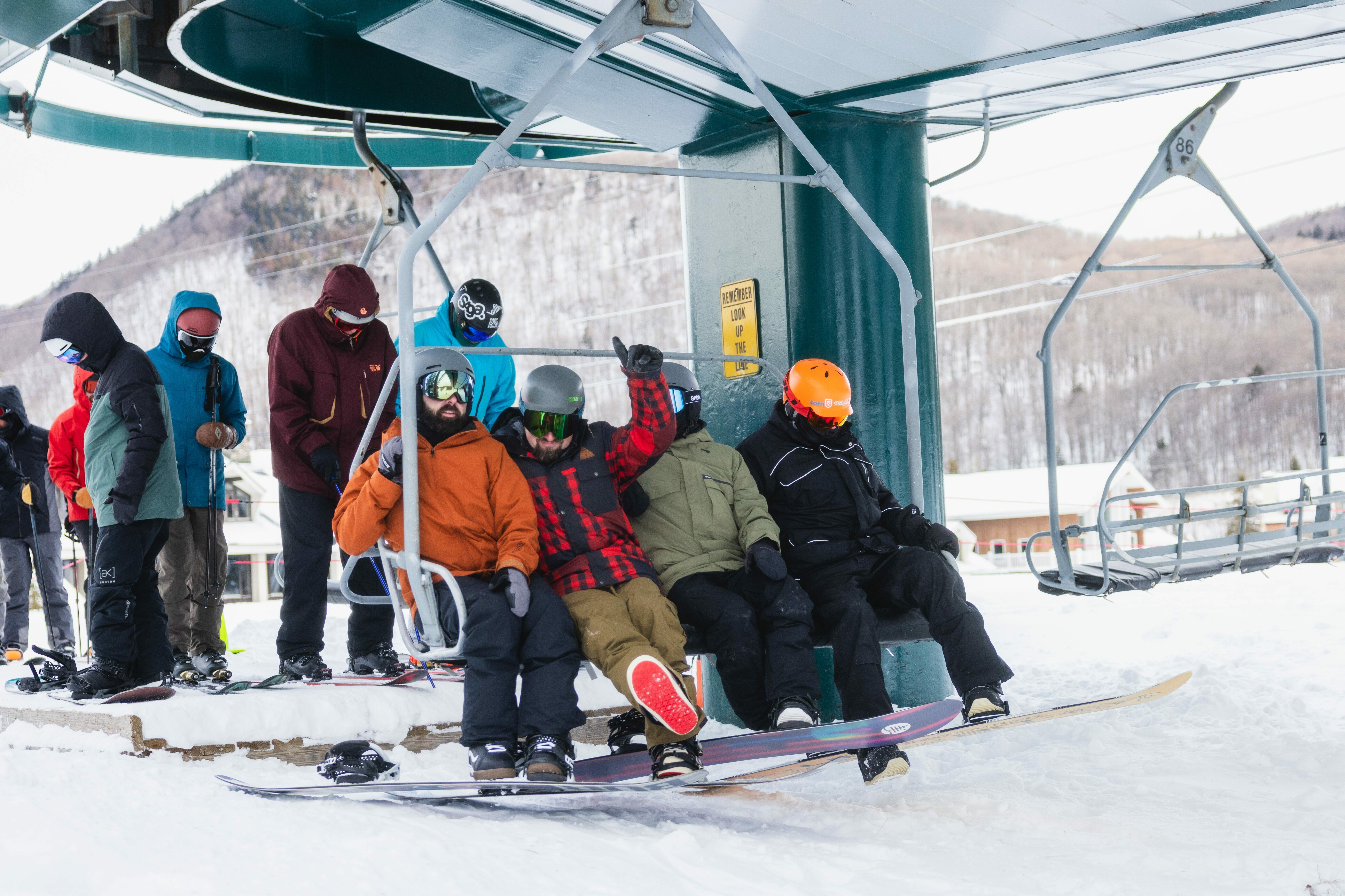 A group of snowboarders seated on a ski lift in a snowy mountain setting.